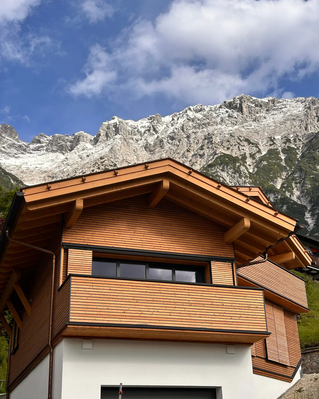 Neu errichtetes Einfamilienhaus mit Holzfassade und Satteldach vor Bergkulisse